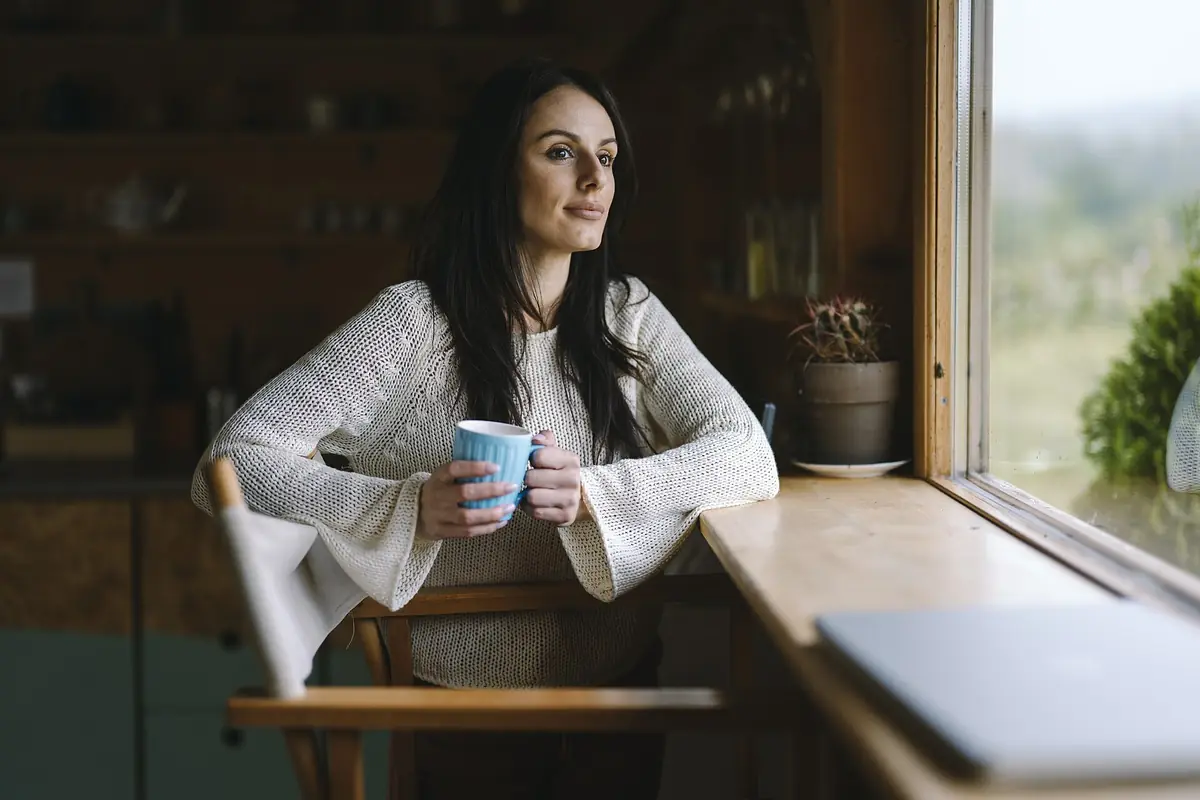 A woman enjoying a hot drink by a sunny window at home