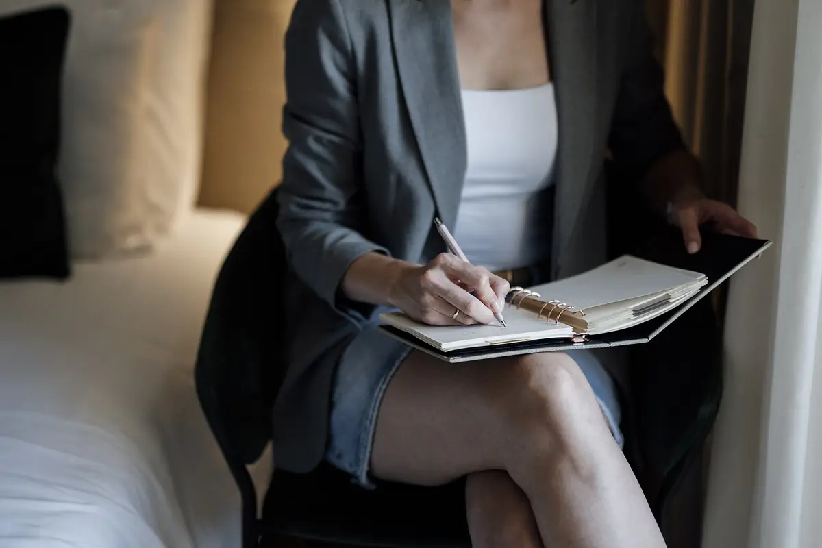A woman writing in a notebook while sitting in a chair at home